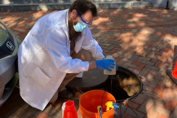 KELLEN SAWYER, A RESEARCH TECHNICIAN LEADING THE UNH SEWAGE MONITORING, RETRIEVES A SAMPLE FROM ONE OF THE MANHOLES