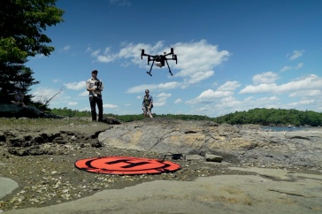 Two people fly a drone on a rocky coast