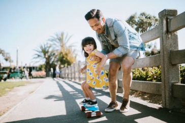 Image of girl learning to skateboard with dad