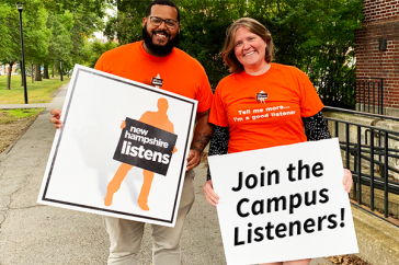 A photo of two New Hampshire Listens staff holding signs encouraging people to join Campus Listeners