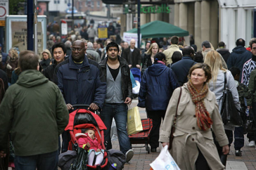 People of different races and ethnicities walk together on a crowded sidewalk.