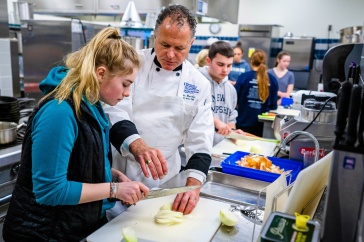 Chef Ron and a young female student work together to cut an onion