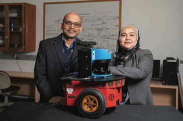 Two researchers stand in front of a red robot