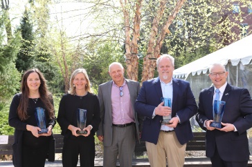 Five people stand side by side, some are holding glass plaques.