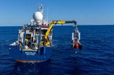 Stern of the Exploration Vessel Nautilus with a crane deploying the DriX autonomous surface vessel into the ocean.