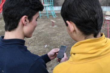 Two boys, seen from behind, look at a smart phone together