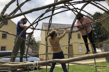 Three people building a wigwam.