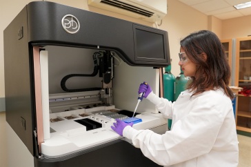 A young woman uses a syringe to add material to a tray with DNA samples