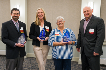 Four people -- two men and two women -- stand holding blue UNH Innovator of the Year awards.