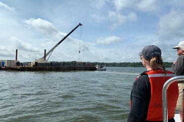 Laura Brown (left), owner of Fox Point Oysters, and Ray Grizzle, a UNH professor of biological sciences, watch as a crane operated by Riverside & Pickering Marine Contractors deposits oyster shells at the Nannie Island reef restoration site.