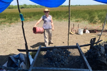 A woman in a striped shirt stands at the edge of a tent on an archaeological site
