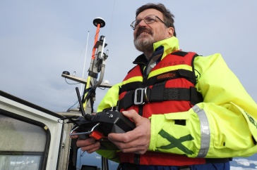 Brian Calder wears a life jacket and holds a remote controller while aboard a boat.
