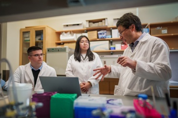 Three scientists wearing white coats work in a lab.