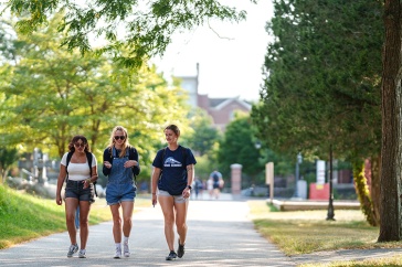 Three female students walk along a path surrounded by green trees
