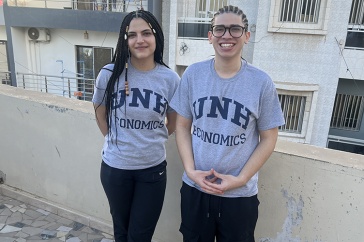 A woman and a man, both wearing UNH economics T-shirts, pose for a photo together