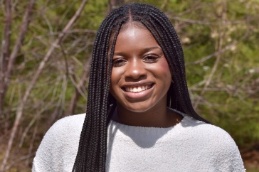 UNH student Leandra Bryant posing outside in gray shirt and blue jeans 