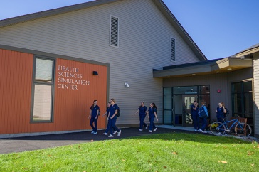 A group of nursing students in blue scrubs walk together outside UNH's Health Sciences Simulation Center