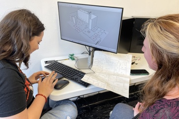 Two female students working at a desk with a computer on it