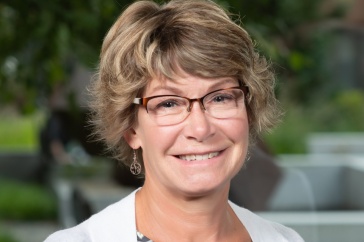 Professional headshot of Karla Armenti, a women with short wavy hair, wearing glasses and a floral blouse.