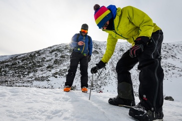 Two researchers in winter gear work on a snowy mountain