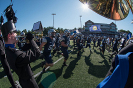 UNH football players and marching band run across the field during the Homecoming 2017 football game