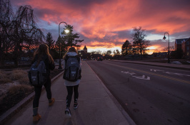 UNH students walking on Garrison Avenue against a colorful sunset over Thompson Hall