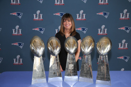 Louise Griffin standing in front of Patriots 5 Super Bowl trophies