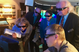 Small group of peope wearing 3D glasses crowd around a computer
