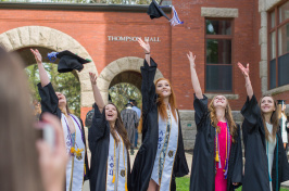 UNH graduates tossing caps in front of Thompson Hall on Durham campus