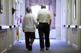 Image of two elderly people walking hand-in-hand down hall