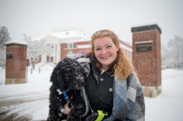 UNH student holding dog on sidewalk in front of Hamilton Smith Hall during snow storm