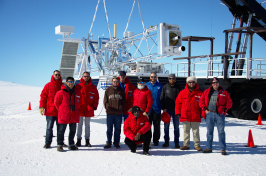 Team of researchers in Antarctica stand in front of a large telescope.