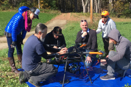 Group of researchers gathers around large drone outside on a sunny day.