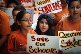 Grade school students wear orange shirts and hold protest signs.