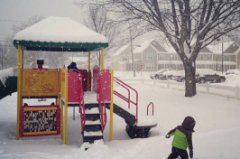 A young child plays on a playground covered in snow.