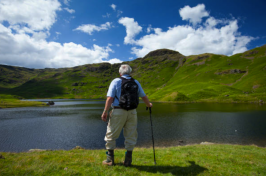 Man stands at the edge of a lake looking at the green rolling hills