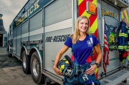 UNH exercise science researcher Deborah Feairheller stands behind a fire truck, dressed in turnout gear