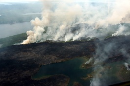 Multiple smoke plumes from wildfires are seen from airplane above mountains and lakes. 