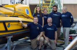 The Autonomous Surface Vehicle team stands next to a yellow vessel.