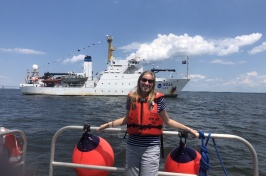 Natalie Cook stands on a ship in front of the Thomas Jefferson hydrographic vessel.