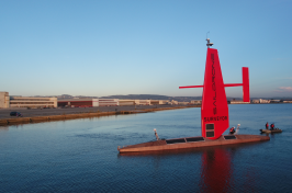 Large red ocean-going vessel sits stationary in a bay.