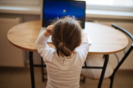 Photo of a young child working on a computer and seated at a table.
