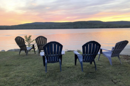 Adirondack chairs sit in front of a lake in Maine