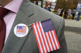 A man in a suit has a NH "I voted sticker" on his chest as well as an American flag