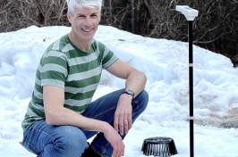 Man in striped shirt crouches in snow next to monitoring equipment