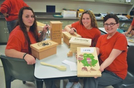 three women in classroom showing their woodworking projects
