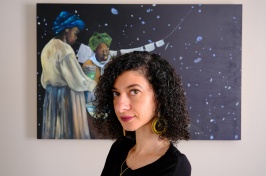 Woman with dark curly hair looks at the camera, painting of Black astronomers behind her