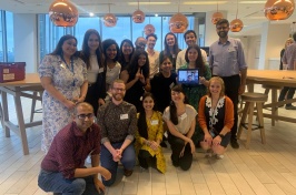 Group of 17 students gather in a well-lit room and smile at the camera.