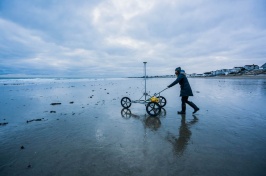 Female student pushes a GPS cart across a beach in winter