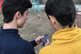 Two boys, seen from behind, look at a smart phone together